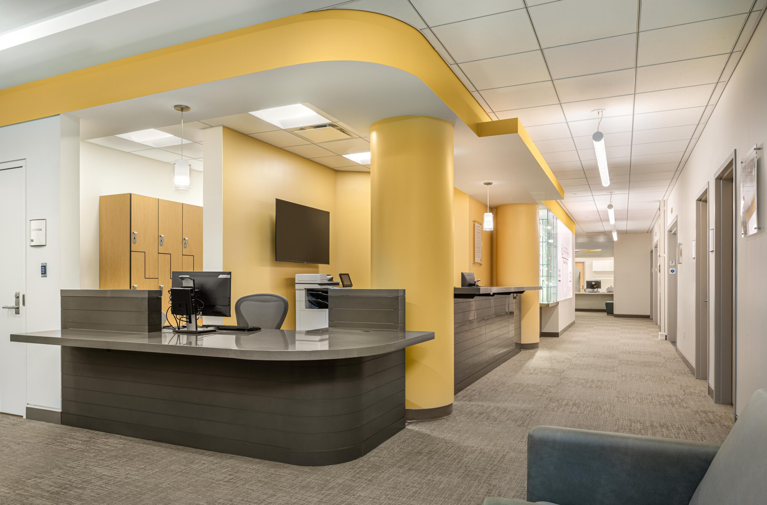 A custom quartzite and solid-surface reception desk sits between painted circular columns, with views to the entrance elevators and main waiting area.