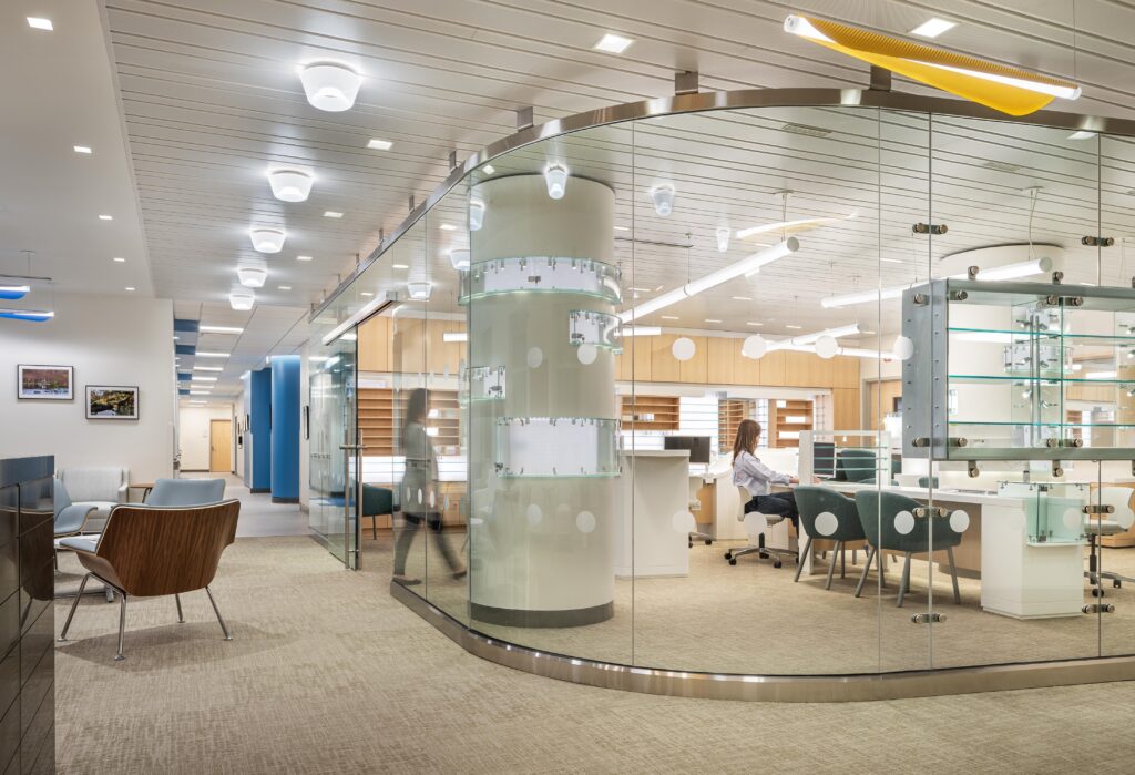 A curved glass wall defines the Optical Retail Area, visible from the corridor and sub-waiting. Displays are built into columns and glass.